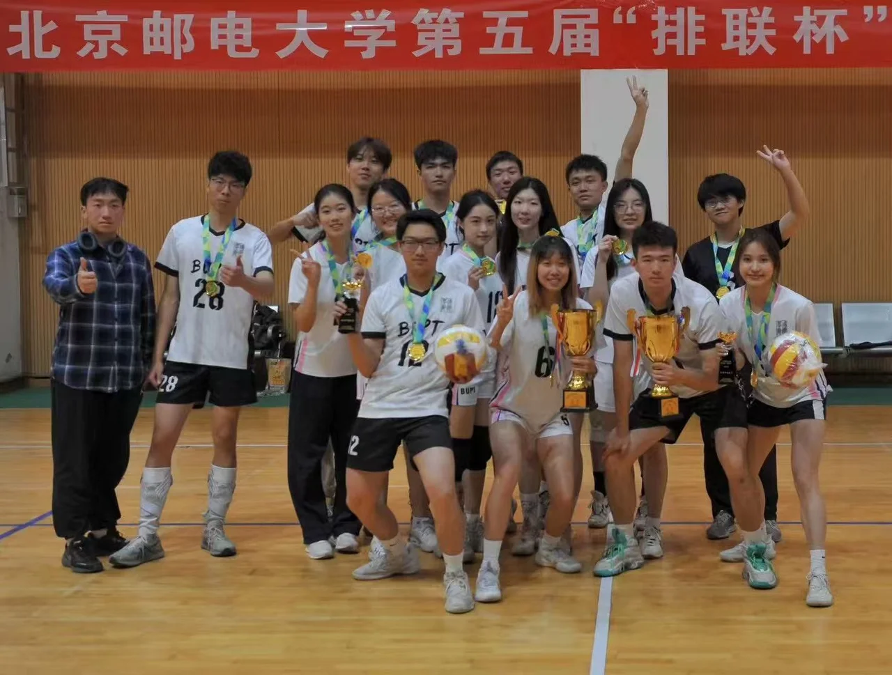 Players and friends in BUPT jerseys wearing medals and posing with trophies and volleyballs