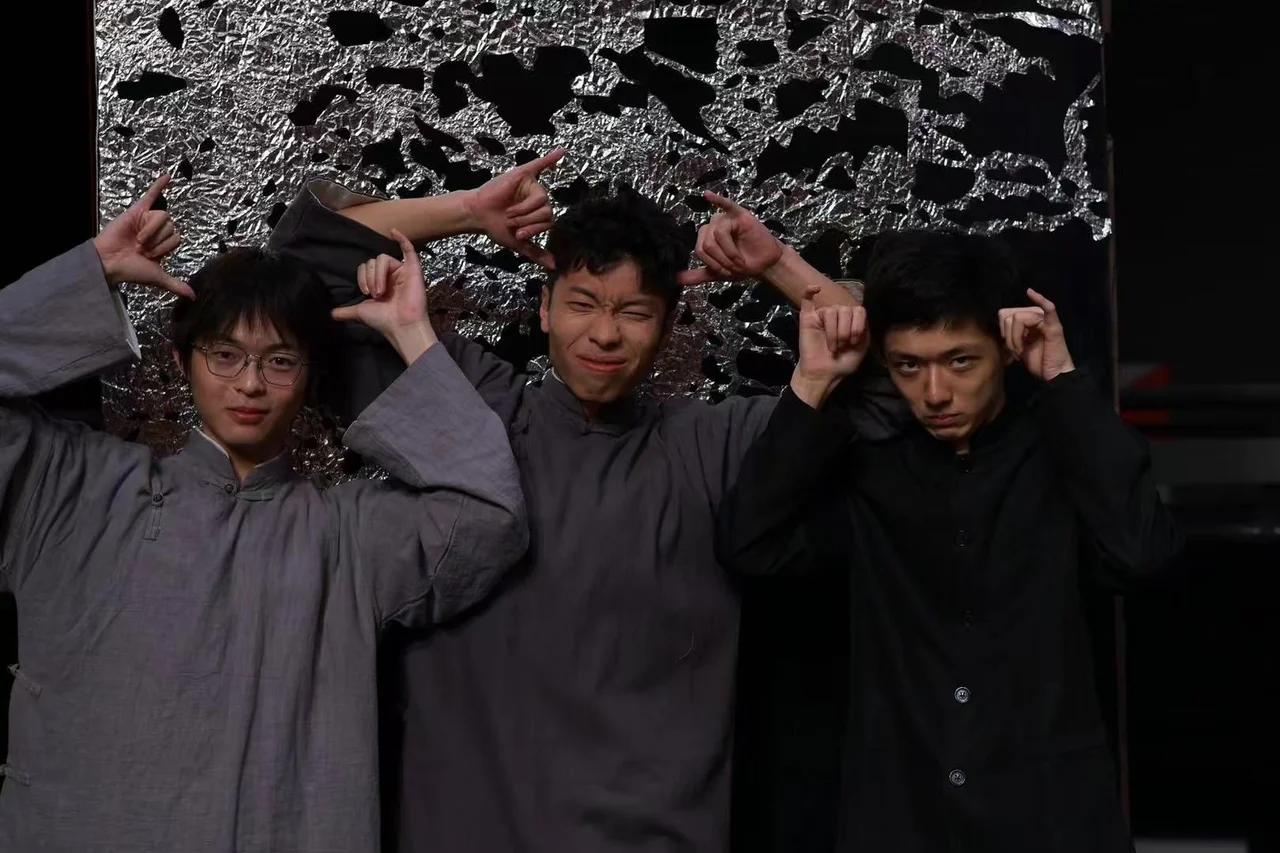 Three friends in costume posing playfully with hand gestures in front of a silver stage set