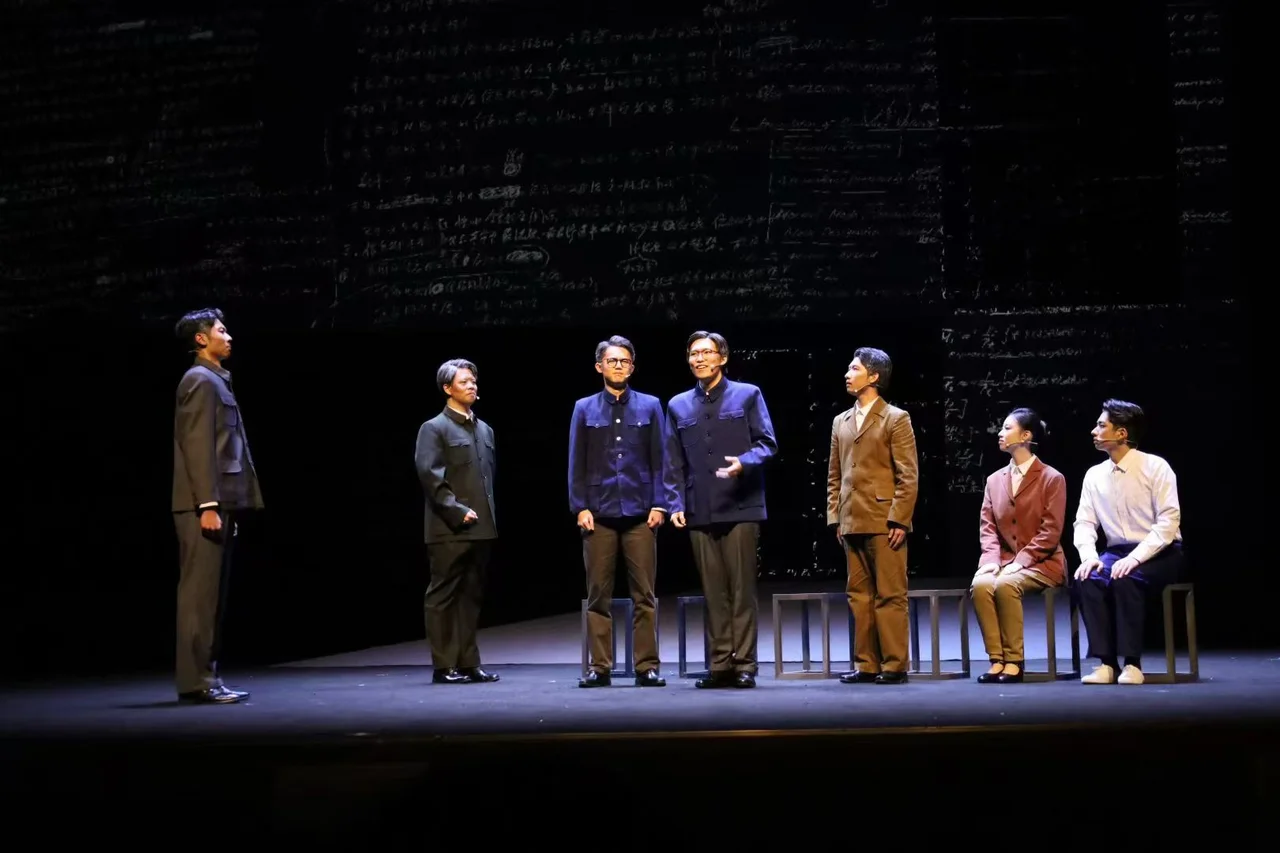 Seven actors standing or seated before a backdrop covered in writing