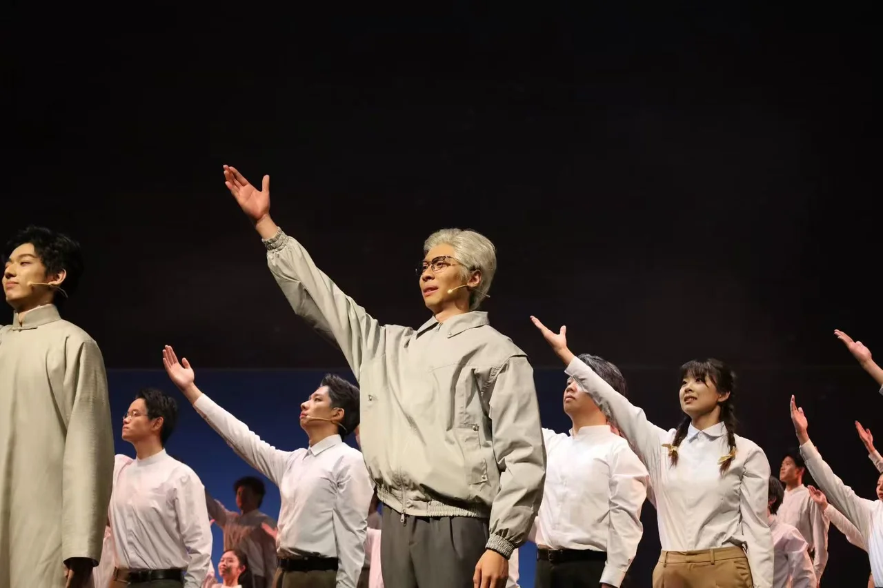 The gray-haired performer and the ensemble raising their arms on stage