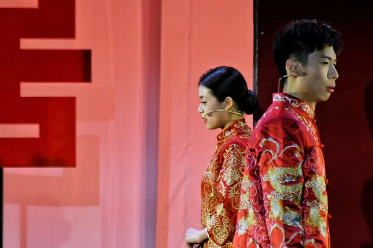Two actors in red wedding costumes standing back to back against the red stage set