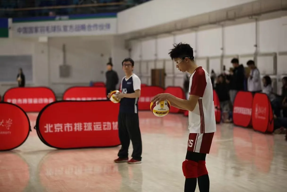 A player in a red-and-white number 15 jersey and sports glasses holding a volleyball on an indoor court