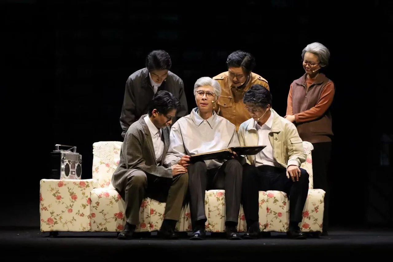 A gray-haired actor looking through an album on a patterned sofa, surrounded by other performers